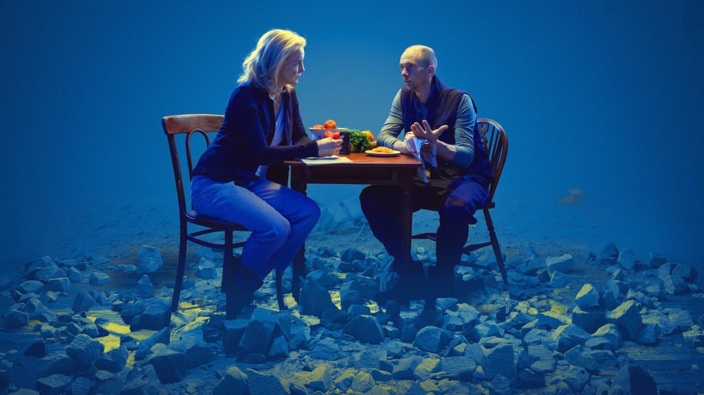 Promotional Image of The Reckoning by Dash Arts featuring Marianne Oldham and Tom Godwin sat at a Kitchen Table in conversation over the preparation of a Ukrainian Summer Salad. Photo by Rich Lakos, Design by Desk Tidy Design